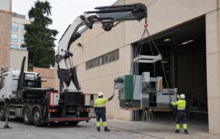 Camión grúa descargando un grupo electrógeno cabinado sobre una base preparada en una instalación industrial